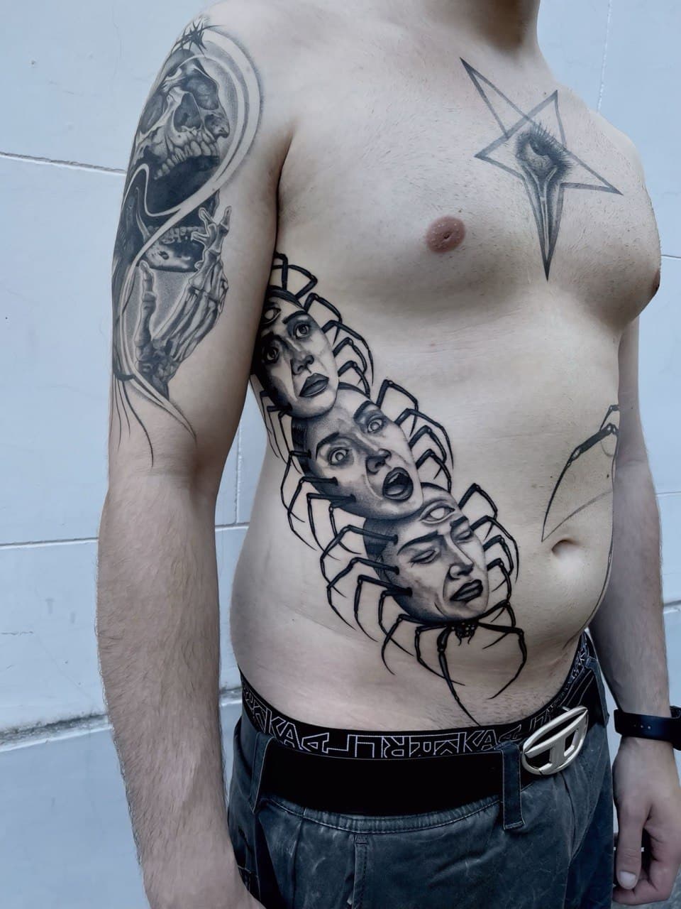 Tatuaggio millepiedi surreale con tre volti umani e terzo occhio Babydrop